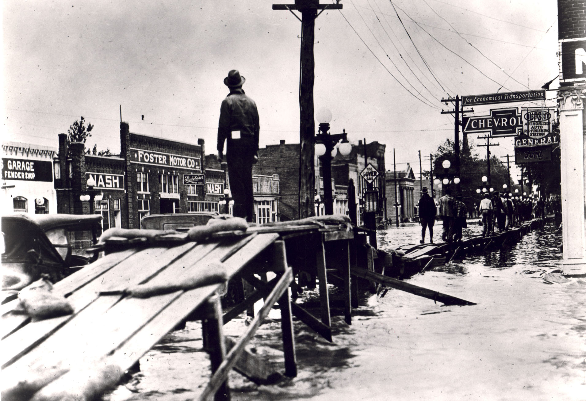 A man stands on raised wooden walkway over flooded streets in a small city A man stands on raised wooden walkway over flooded streets in a small city