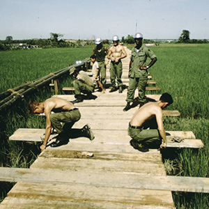 Several soldiers building a wooden platform across a green field