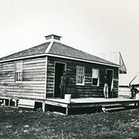 Crude square wooden building with men standing on its wooden porch