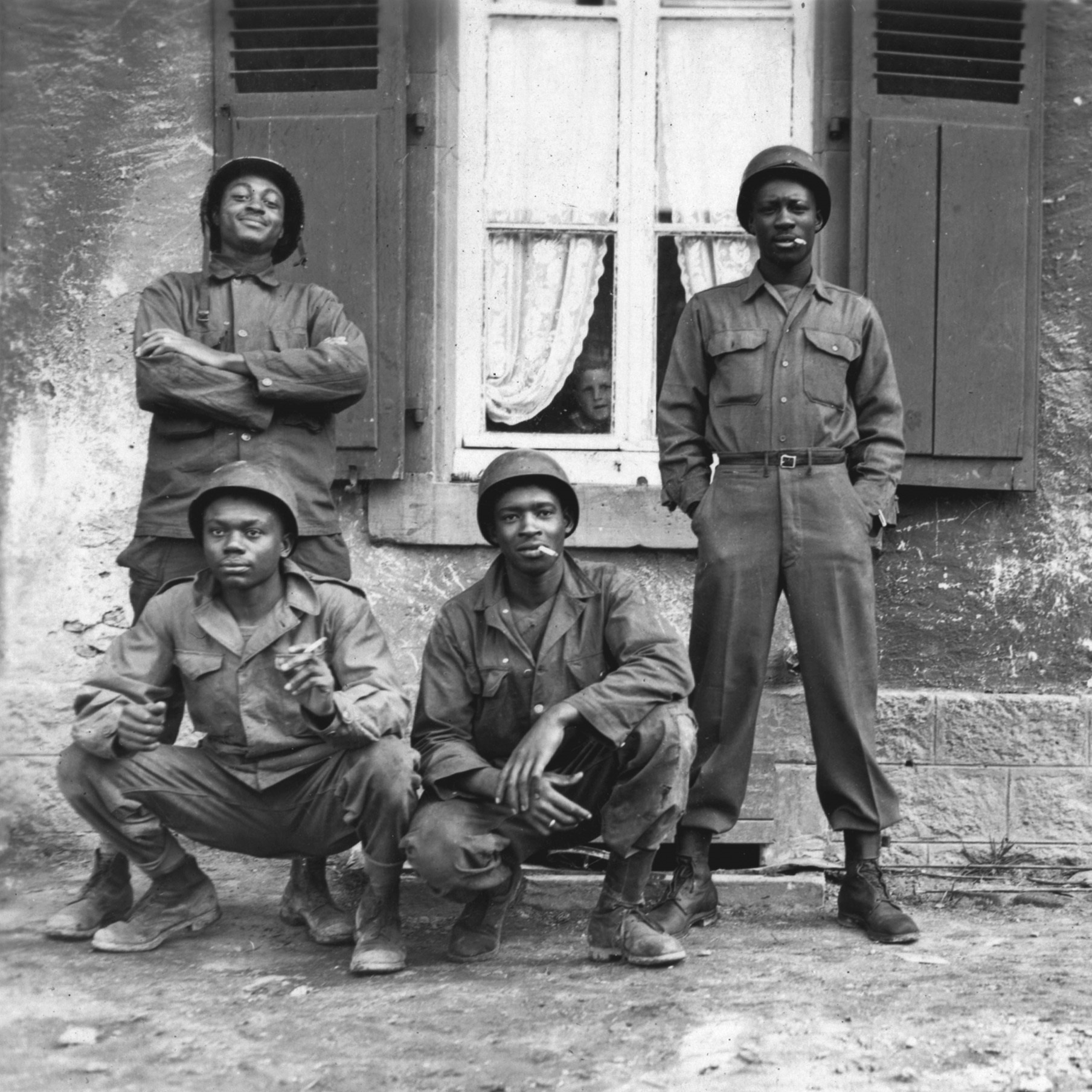 Four soldiers pose outside a window with a child within peering out