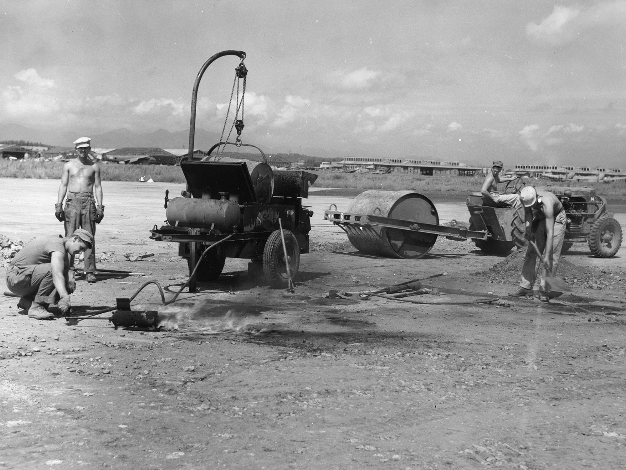 Four men with small heavy equipment paving a runway