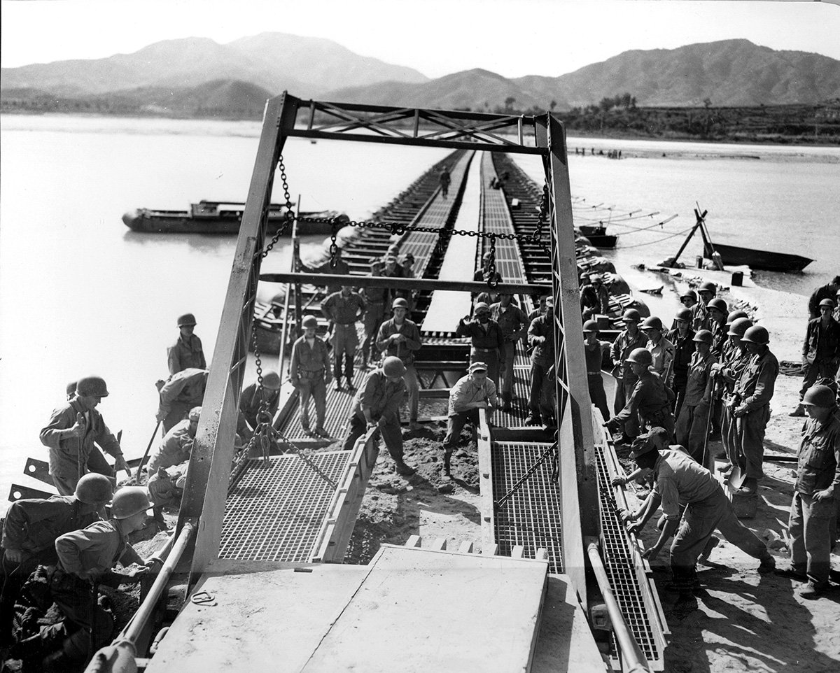 soldiers repairing a long bridge resting on pontons over a wide river