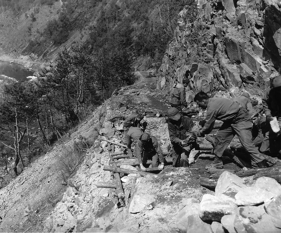 soldiers on a steep mountainside repair a roadway with stone