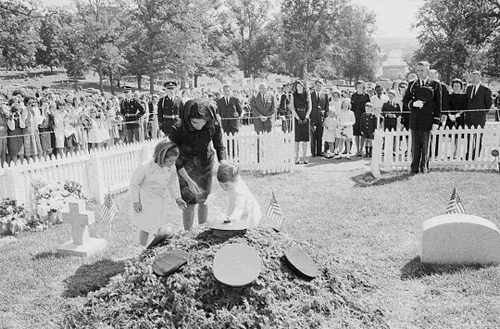 Caroline, Jacqueline, and John F. Kennedy, Jr., place flowers at the base of the eternal flame
