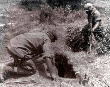 A soldier from the 8th Engineer Battalion, 1st Cavalry Division, prepares to enter a tunnel while an armed soldier keeps guard