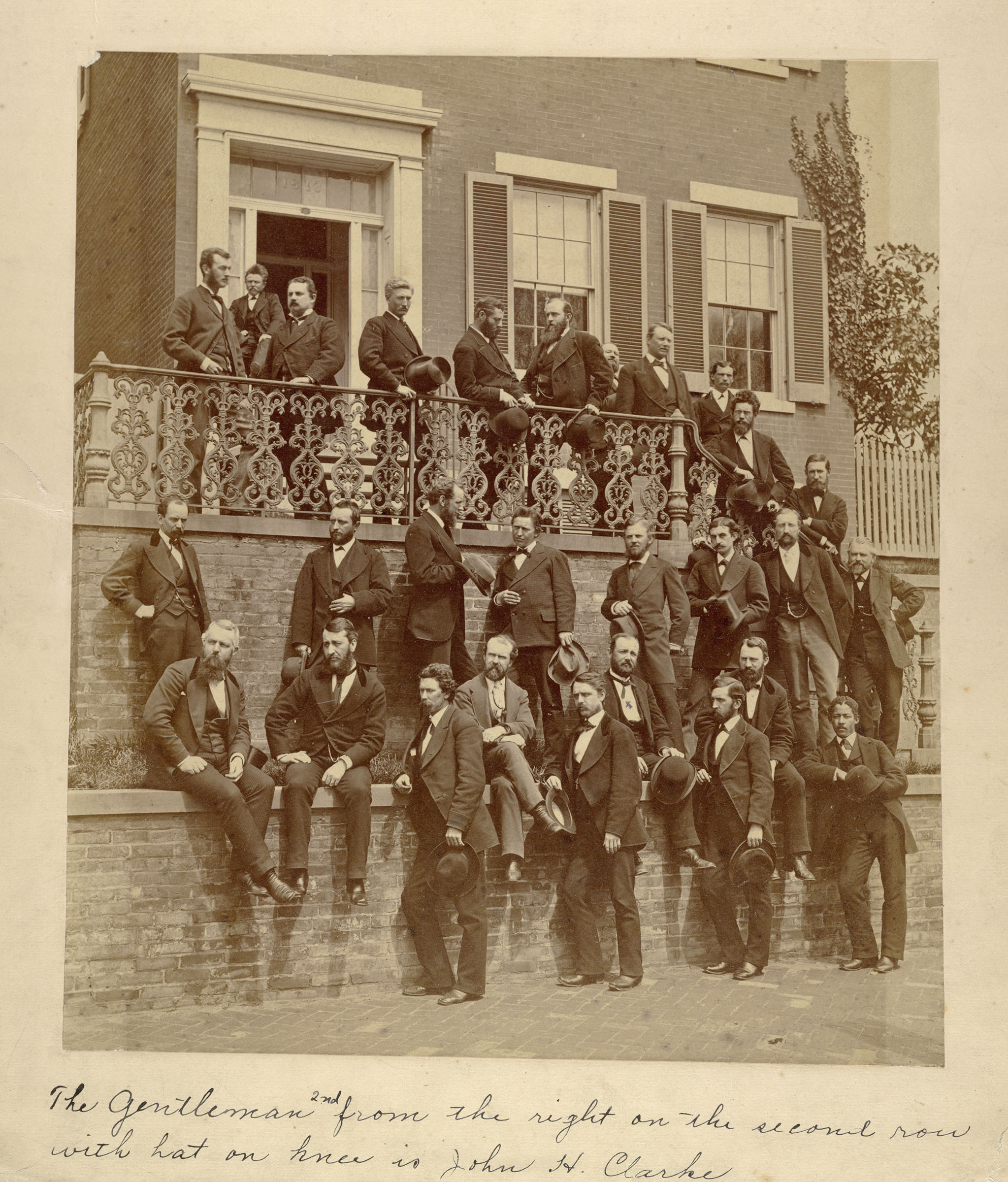 Group of men in suits arranged around an outside porch and grounds Group of men in suits arranged around an outside porch and grounds