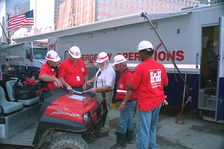 People in red usace shirts and hard hats at a mobile communications trailer