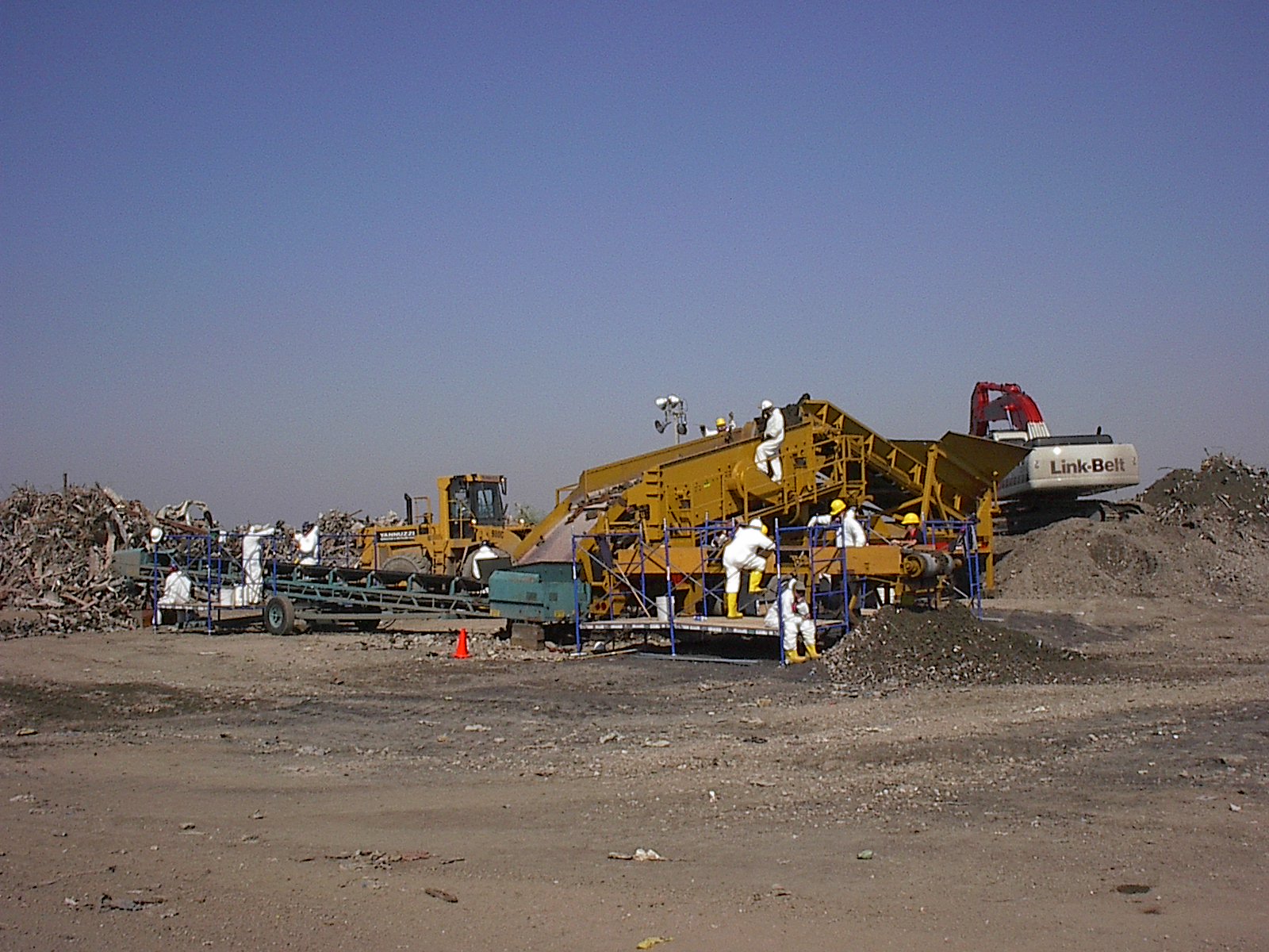 workers in white use machinery to sort debris