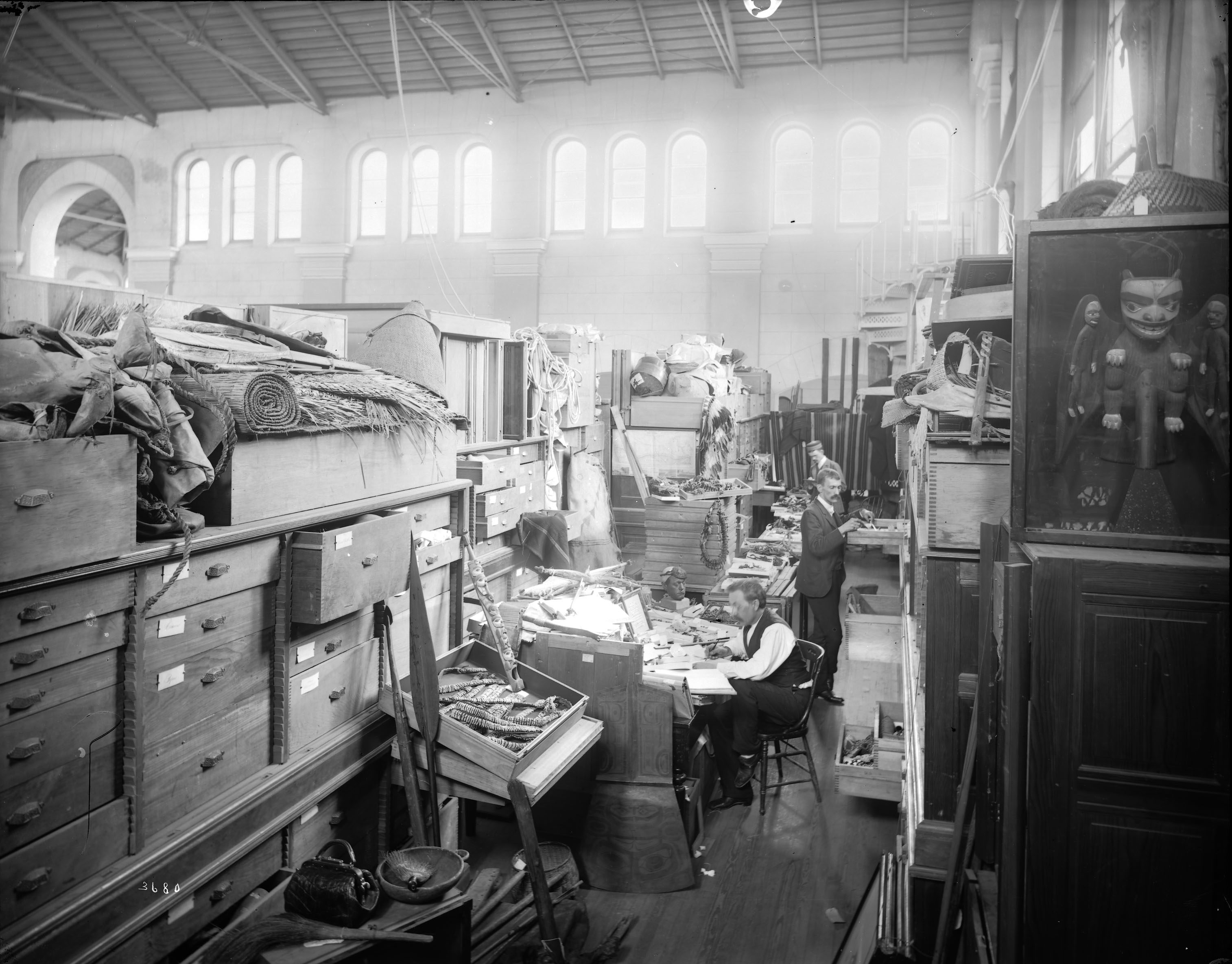 Two men working in a large room filled with boxes and crates