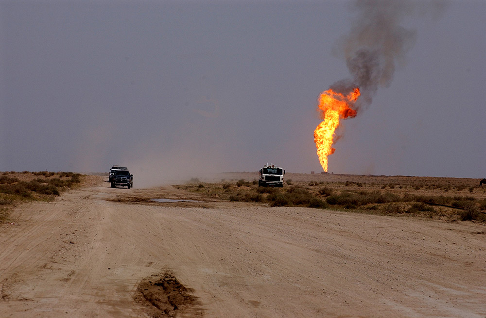 Flames shoot from a burning oil well in the sandy distance